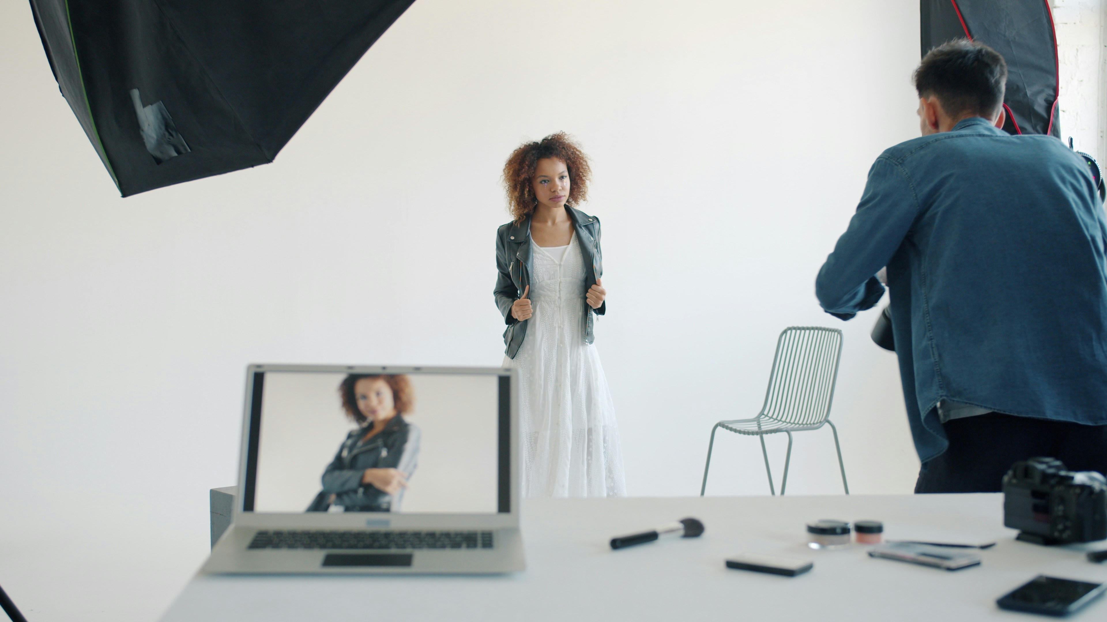 Beautiful young lady is posing for camera during photo shoot in studio with photographer. Modern technology, occupation and youth lifestyle concept.